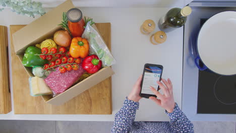 Overhead-shot-of-woman-in-kitchen-with-fresh-ingredients-looking-at-online-recipe-on-mobile-phone---shot-in-slow-motion