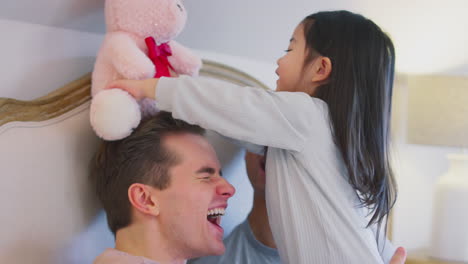 Family-With-Two-Dads-In-Bed-At-Home-Playing-Game-With-Daughter-And-Her-Soft-Toy