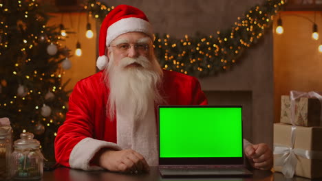 Santa-holds-a-laptop-with-a-green-screen-while-sitting-in-the-Christmas-decorations.-High-quality-4k-footage