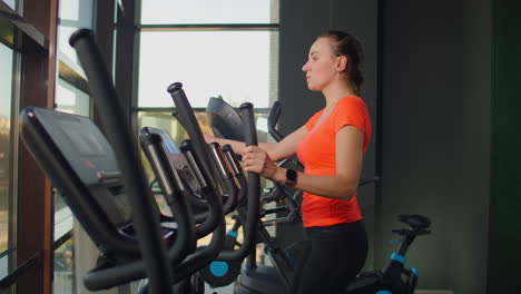 Beautiful-fit-sportive-positive-young-woman-in-gym-doing-exercises-on-elliptical-trainer-working-out