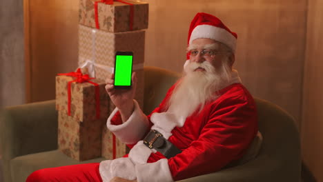 Der-Weihnachtsmann-Zeigt-Mit-Dem-Finger-Auf-Den-Grünen-Bildschirm-Des-Mobiltelefons.-Weihnachtsverkauf.-Der-ältere-Weihnachtsmann-Zeigt-Einen-Bildschirm-Mit-Einem-Chromakey.-Hochwertiges-4K-Filmmaterial