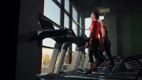 A-group-of-people-walking-on-treadmills-near-a-large-panoramic-window.-Group-cardio-workout.-Start-of-fitness-classes.-Young-beautiful-women-and-men-in-sportswear-in-cardio-fitness-room.