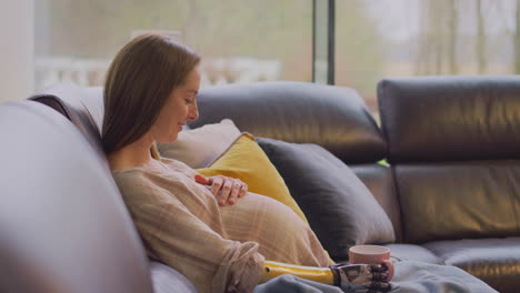 Schwangere-Frau-Mit-Armprothese-Sitzt-Entspannt-Zu-Hause-Auf-Dem-Sofa-Und-Trinkt-Ein-Heißes-Getränk