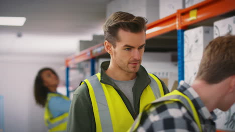 Male-Team-Leader-With-Digital-Tablet-In-Warehouse-Training-Intern-Standing-By-Shelves