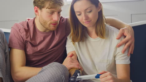 Disappointed-Couple-With-Woman-With-Prosthetic-Arm-Sitting-In-Bathroom-With-Negative-Pregnancy-Test
