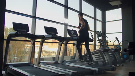 Junge-Sportliche-Männer-Und-Frauen-Trainieren-Und-Laufen-Auf-Dem-Laufband-Im-Fitnessstudio.-Zeitlupe-In-Der-Nähe-Eines-Großen-Panoramafensters