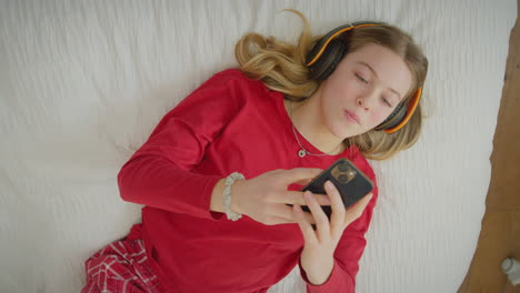 Blick-Von-Oben-Auf-Ein-Teenager-Mädchen-Mit-Drahtlosen-Kopfhörern,-Das-Musik-Oder-Filme-Vom-Mobiltelefon-Streamt-–-Heiß-In-Zeitlupe