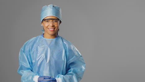 Portrait-Of-Smiling-Female-Surgeon-Wearing-Safety-Glasses-And-Against-Grey-Background
