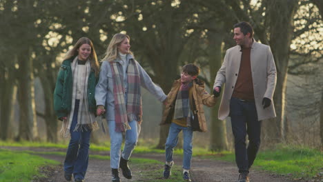 Full-length-shot-of-family-holding-hands-on-walk-through-autumn-countryside-together---shot-in-slow-motion