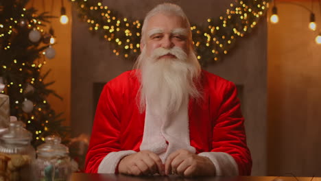 Der-Weihnachtsmann-Sitzt-An-Einem-Tisch-In-Einem-Schönen-Wohnzimmer,-Das-Für-Ein-Frohes-Weihnachtsfest-Dekoriert-Ist.-Der-Weihnachtsmann-Lächelte-Und-Nickte-Zustimmend.-Hochwertiges-4K-Filmmaterial