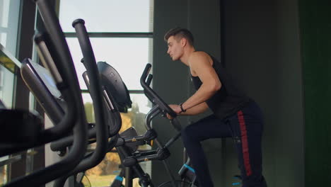 Beautiful-fit-sportive-positive-young-man-in-gym-doing-exercises-on-elliptical-trainer-working-out.