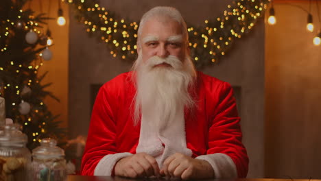 Headshot-Looking-at-the-camera-Happy-old-bearded-Santa-Claus-wearing-costume-and-waving-hand-video-calling-recording-video-Merry-Christmas-greeting-face-camera-view.-High-quality-4k-footage