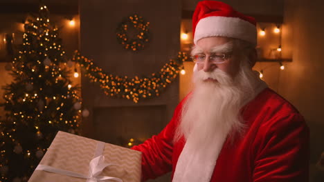 Der-Weihnachtsmann-Hält-Und-Schüttelt-Eine-Große-Schöne-Schachtel-Mit-Einem-Geschenk-Für-Ein-Gehorsames-Kind-Für-Ein-Frohes-Weihnachtsfest.-Schaut-In-Die-Kamera-Und-Lächelt.-Mittlere-Aufnahme.-Hochwertiges-4K-Filmmaterial