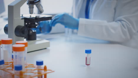 Close-Up-Of-Lab-Worker-Conducting-Research-Using-Microscope-Holding-Blood-Sample--With-Blank-Label