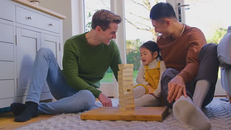 Familie-Mit-Zwei-Vätern-Spielt-Mit-Ihrer-Tochter-Zu-Hause-Und-Stapelt-Holzsteine-In-Einen-Turm