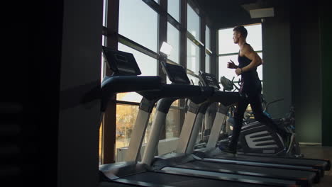 Young-athletic-men-and-women-exercising-and-running-on-treadmill-in-sport-gym.-Slow-motion-Near-a-large-panoramic-window
