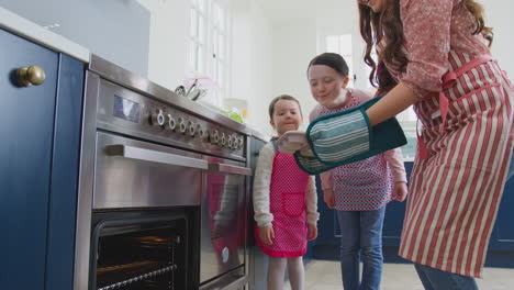 Mother-And-Daughters-Taking-Freshly-Baked-Cupcakes-Out-Of-The-Oven-In-Kitchen-At-Home-Together