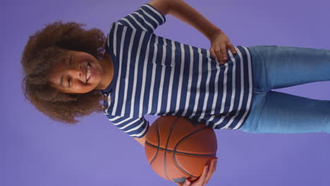 Vertikales-Video-Eines-Lächelnden-Jungen,-Der-Basketball-Vor-Violettem-Hintergrund-Hält