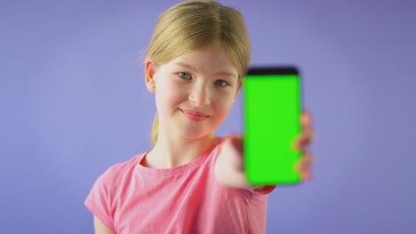 Studioporträt-Eines-Mädchens,-Das-Ein-Mobiltelefon-Mit-Grünem-Bildschirm-Vor-Violettem-Hintergrund-Benutzt