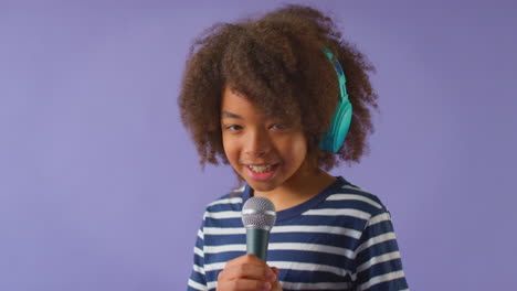 Studio-Shot-Of-Boy-Wearing-Headphones-Singing-Karaoke-Into-Microphone-Against-Purple-Background