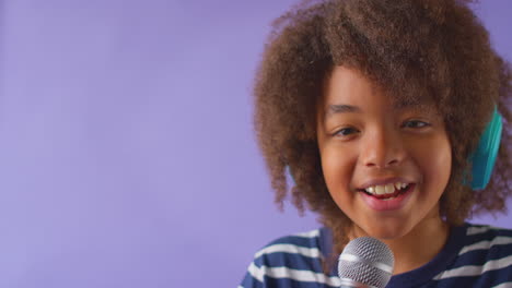 Studio-Shot-Of-Boy-Wearing-Headphones-Singing-Karaoke-Into-Microphone-Against-Purple-Background