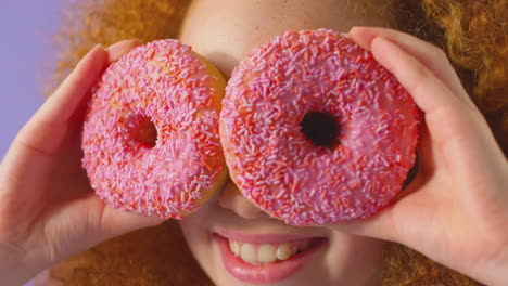 Nahaufnahme-Eines-Mädchens,-Das-Vor-Violettem-Hintergrund-Zwei-Donuts-Vor-Augen-Hält