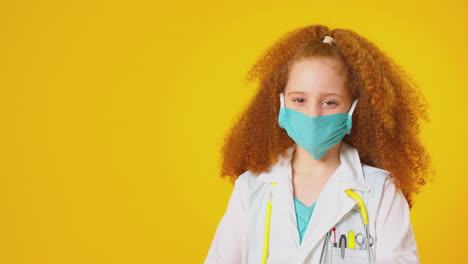 Studioporträt-Eines-Als-Arzt-Oder-Chirurg-Verkleideten-Mädchens-Mit-Gesichtsmaske-Vor-Gelbem-Hintergrund