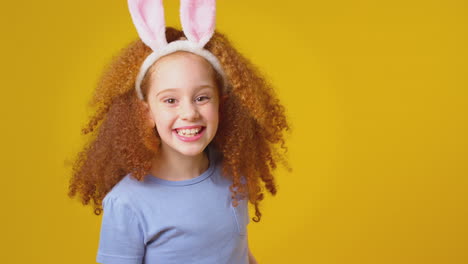 Studio-Shot-Of-Girl-Wearing-Rabbit-Ears-Jumping-Up-from-Bottom-Of-Frame-Against-Yellow-Background