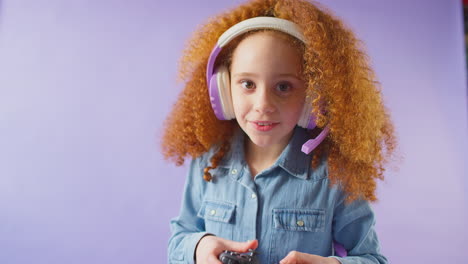 Studio-Shot-Of-Girl-Wearing-Headset-Gaming-With-Controller-Against-Purple-Background