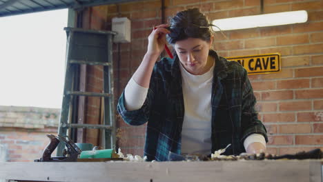 Young-Female-Carpenter-Drawing-And-Measuring-Woodwork-Design-In-Garage-Workshop
