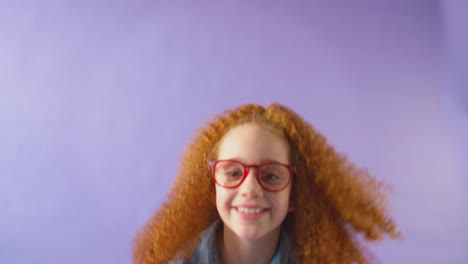 Studioaufnahme-Eines-Jungen-Mädchens-Mit-Roten-Haaren-Und-Brille,-Das-Vor-Violettem-Hintergrund-Springt