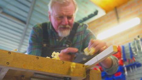 Close-Up-Of-Senior-Male-Carpenter-In-Garage-Workshop-Planing-Piece-Of-Wood
