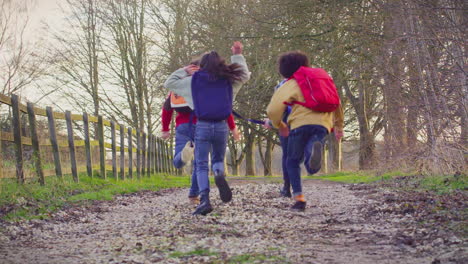 Rear-View-Of--Children-With-School-Backpacks-Outdoors-Running-Along-Countryside-Track