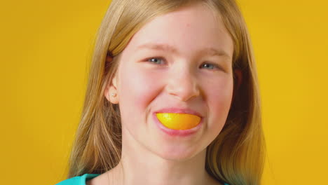 Studio-Portrait-Of-Girl-Using-Orange-Segment-For-Mouth-And-Teeth-Against-Yellow-Background