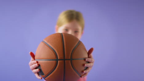 Studioaufnahme-Eines-Jungen-Mädchens,-Das-Basketball-Vor-Violettem-Hintergrund-In-Richtung-Kamera-Hält