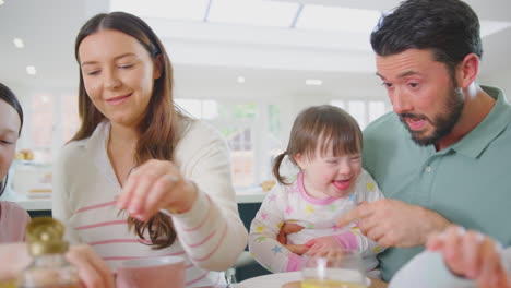 Familie-Mit-Down-Syndrom-Tochter-Sitzt-Zu-Hause-Am-Tisch-Und-Frühstückt