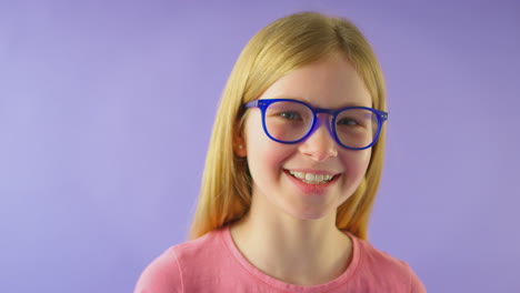 Studio-Shot-Of-Smiling-Girl-With-Long-Hair-Wearing-Blue-Glasses-Against-Purple-Background