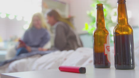 Zwei-Mädchen-Im-Teenageralter-Im-Schlafzimmer-Mit-Bierflaschen-Und-Einem-E-Zigarettenstift-Im-Vordergrund