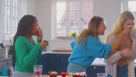 Group-Of-Teenage-Girls-Eating-And-Having-Fun-Playing-With-Cupcakes-In-Kitchen-At-Home