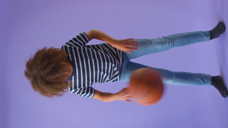 Vertikales-Video-Eines-Jungen,-Der-Mit-Basketball-Vor-Violettem-Hintergrund-Dribbelt
