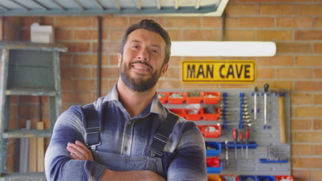 Portrait-Of-Smiling-Man-Wearing-Overalls-In-Garage-Workshop-At-Home