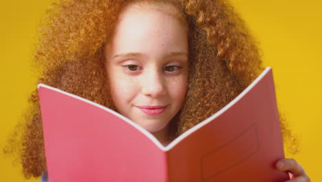 Studio-Shot-Of-Young-Girl-Studying-School-Exercise-Book-Against-Yellow-Background