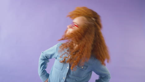 Studioaufnahme-Eines-Jungen-Mädchens-Mit-Roten-Haaren-Und-Brille,-Das-Vor-Violettem-Hintergrund-Die-Haare-Schüttelt