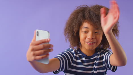 Studio-Portrait-Of-Boy-Waving-Making-Video-Call-On-Mobile-Phone-Against-Purple-Background