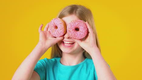 Studioporträt-Eines-Mädchens,-Das-Vor-Gelbem-Hintergrund-Zwei-Donuts-Vor-Augen-Hält