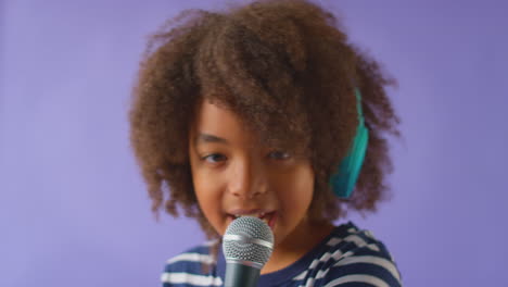 Studioaufnahme-Eines-Jungen-Mit-Kopfhörern,-Der-Vor-Violettem-Hintergrund-Karaoke-Ins-Mikrofon-Singt