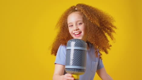 Studioaufnahme-Eines-Mädchens,-Das-Vor-Gelbem-Hintergrund-Karaoke-In-Ein-Aufblasbares-Mikrofon-Singt