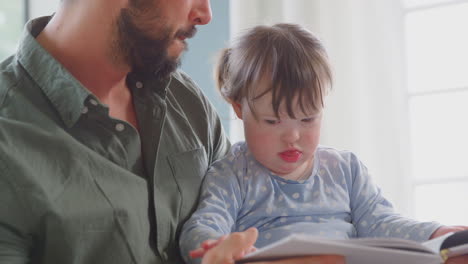 Close-Up-Of-Father-With-Down-Syndrome-Daughter-Reading-Book-And-Laughing-At-Home-Together