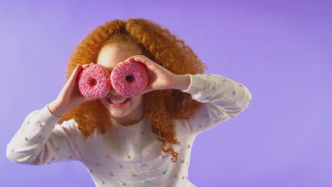 Studioporträt-Eines-Mädchens,-Das-Vor-Violettem-Hintergrund-Zwei-Donuts-Vor-Augen-Hält