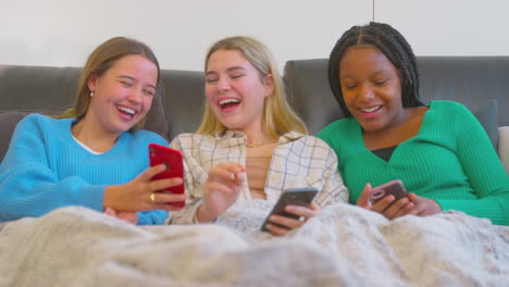 Eine-Gruppe-Multikultureller-Teenager-Freundinnen-Kuschelte-Sich-Unter-Eine-Decke-Und-Schaute-Zu-Hause-Auf-Mobiltelefone
